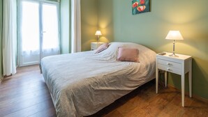 Un dormitorio con una cama, dos mesitas de noche, una lámpara de noche, un cuadro y una puerta.
