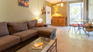 Una sala de estar con un sofá marrón, una mesa de centro de vidrio, una zona de comedor con una mesa y sillas de vidrio, y vistas al exterior.