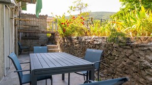 Un patio con mesa y sillas, un muro de piedra y vistas a zonas verdes y colinas.
