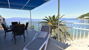 Ein Balkon mit Tisch, Stühlen und Liege, mit Blick auf Meer und Berge.