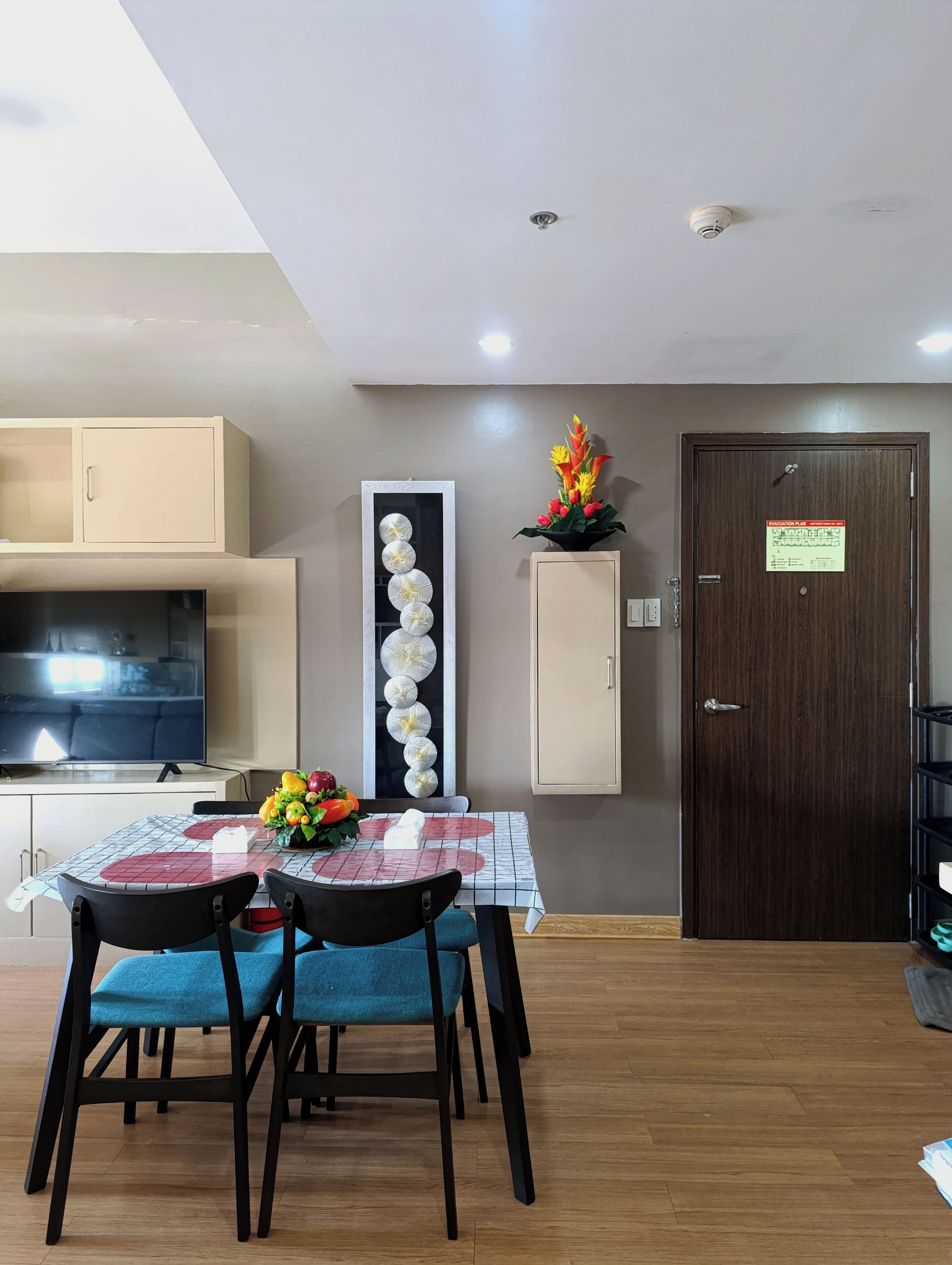 Uma sala de jantar com uma mesa posta para dois, uma televisão e um objeto decorativo na parede.