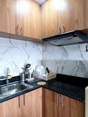 Een keuken met houten kastjes, een zwart aanrecht, een spoelbak en een spatwand met een marmerprint.