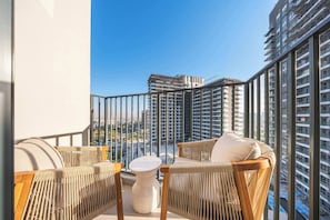 Ein Balkon mit Korbmöbeln, einem weißen Tisch und Blick auf hohe Gebäude.