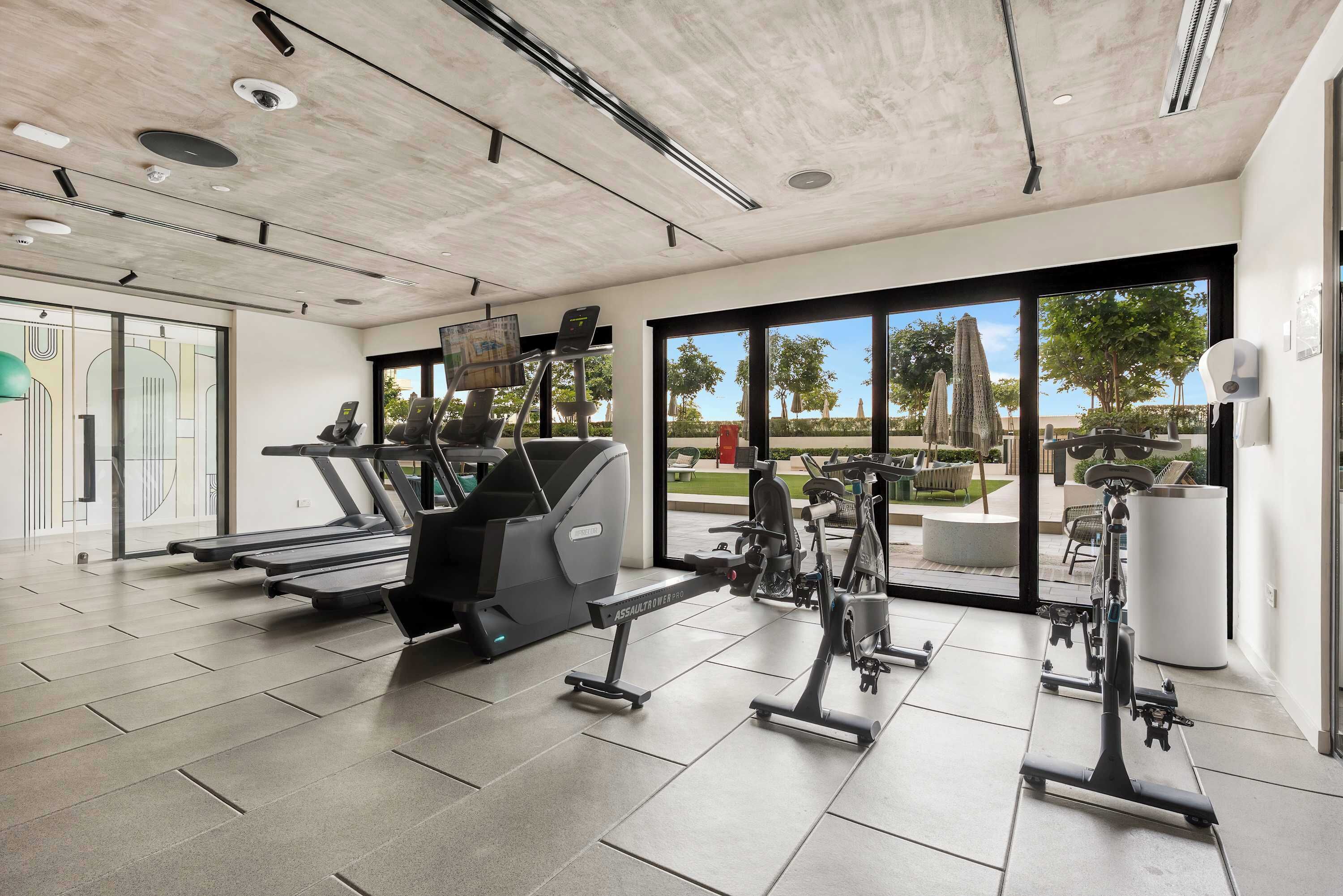 A modern gym with treadmills, elliptical machines, and free weights, large windows with a view of the outdoors, and a clean, minimalist design.