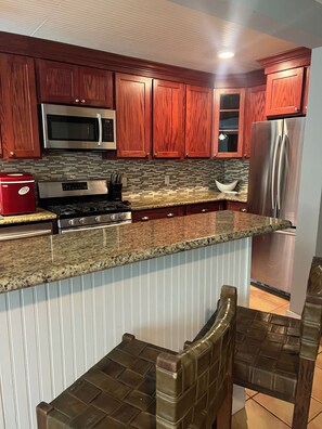 Una cocina con armarios de madera, electrodomésticos de acero inoxidable, encimera de granito y una zona de bar con taburetes.