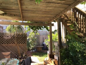 A covered patio area with a wooden pergola, a lattice fence, and a small table. - Paradise Pool House (Galveston)