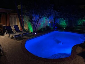 A swimming pool with a curved edge, surrounded by lounge chairs and a tree. - Paradise Pool House (Galveston)