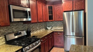 A kitchen with wooden cabinets, stainless steel appliances, and a tiled backsplash. - Paradise Pool House (Galveston)