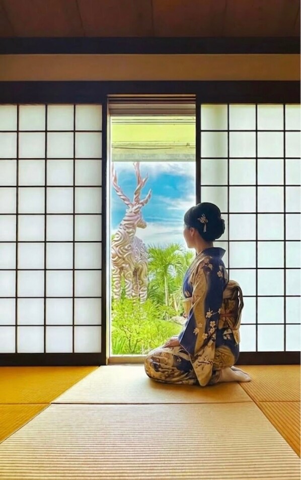 A room with tatami flooring, a sliding door with a view of greenery, and a traditional Japanese-style decor.