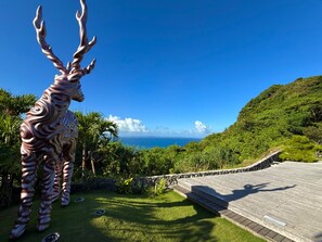 A sculpture of a deer-like figure in a garden with a view of the ocean.