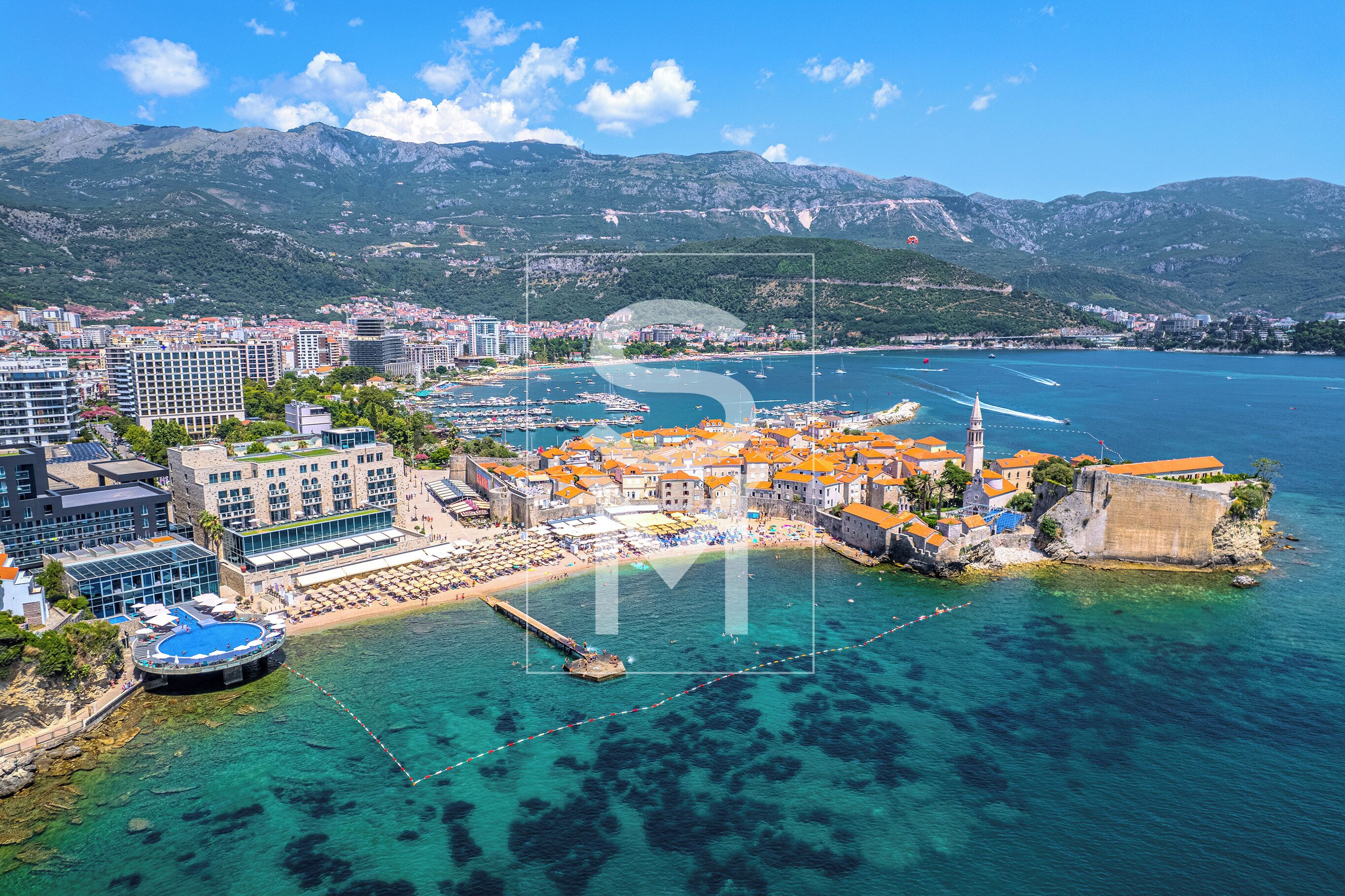 An aerial view of a coastal town with buildings, a marina, and clear blue waters.