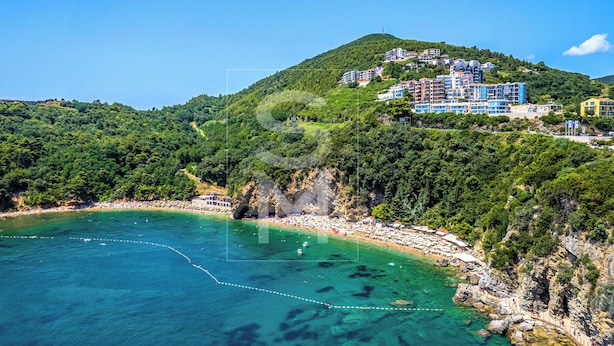 Uma área costeira com praia, montanha com edifícios e água azul cristalina.