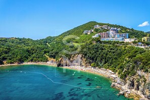 A coastal area with a beach, a mountain with buildings, and clear blue water. - Status M Apartments Adok23 (Budva)