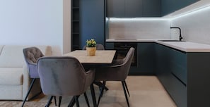 Eine moderne Küche mit dunklen Schränken, einem eingebauten Backofen und einer kleinen Essecke mit zwei Stühlen und einem Tisch.
