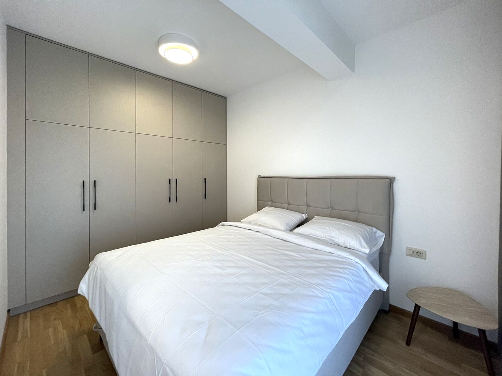 Un dormitorio con cama, armario, una mesa redonda e iluminación en el techo.