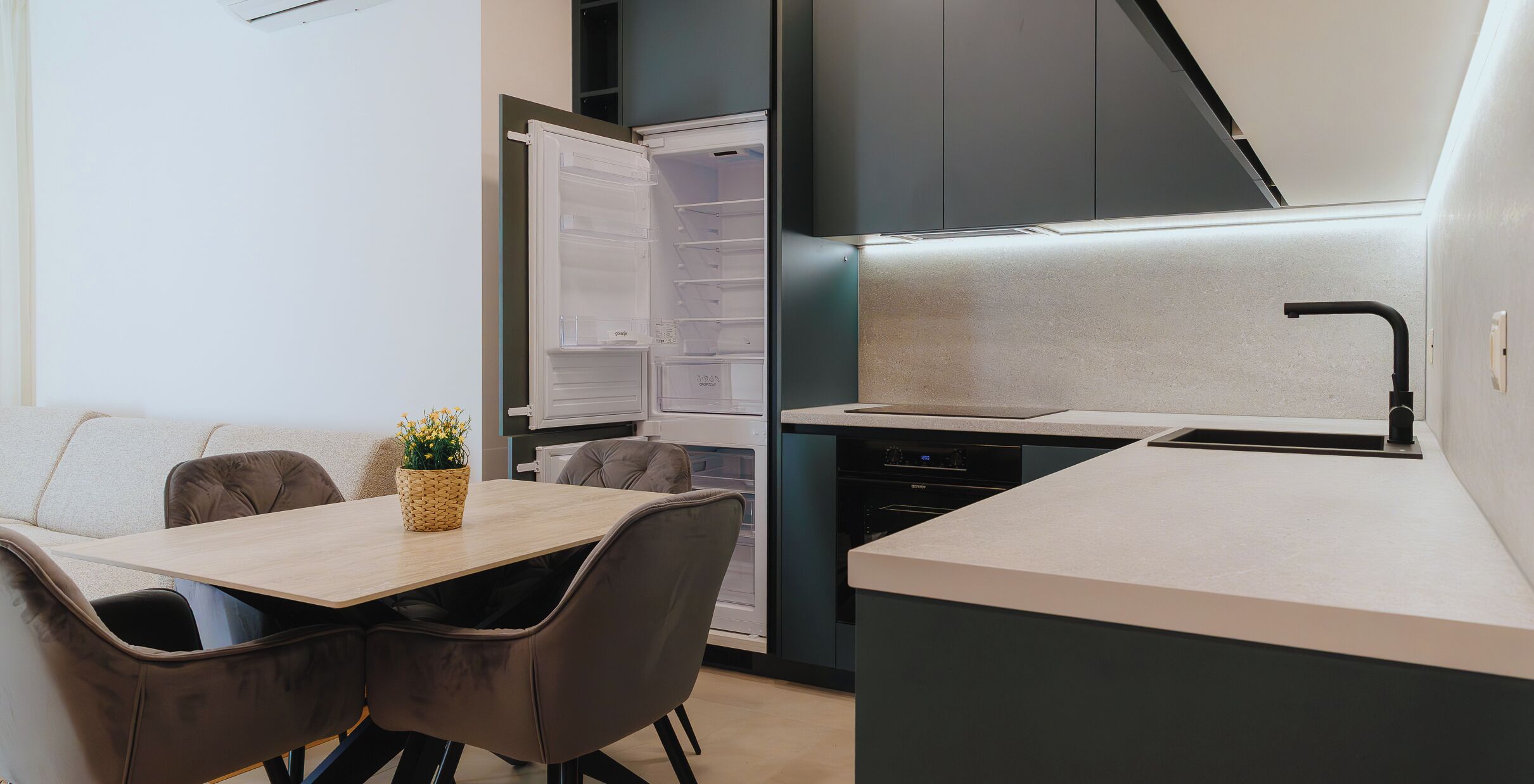 A compact kitchen with a built-in refrigerator, a dining area with a table and chairs, and a small oven.
