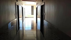 A corridor with doors on both sides, leading to a bright area with a window.