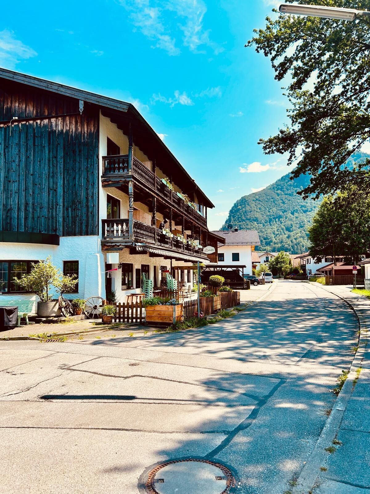 Ein traditionelles Holzhaus mit Balkon, einer Straße davor und einem Berg im Hintergrund.