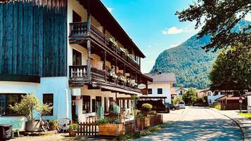 Ein traditionelles Holzhaus mit Balkon, einer Straße davor und einem Berg im Hintergrund.