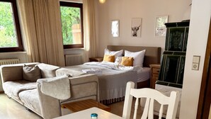 Una habitación de hotel con cama, sofá, mesa de comedor y un florero, además de un minibar.