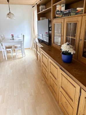 Une cuisine avec des meubles de rangement en bois, une table à manger avec des chaises, un vase bleu rempli de fleurs et un luminaire suspendu.