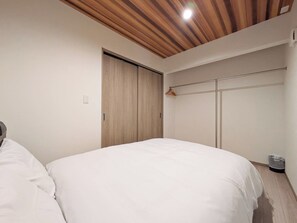 Ein Schlafzimmer mit Holzboden, einem Kleiderschrank, einem Bett mit weißer Bettwäsche und einem Kleiderhaken an der Wand.