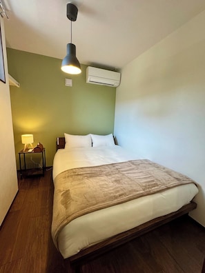 Et hotelværelse med en seng, et natbord med en lampe, et klimaanlæg og trægulv.