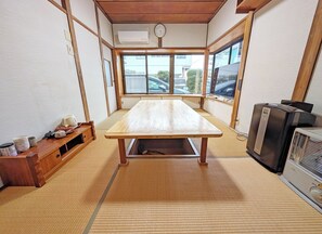 Um quarto com piso de tatame, uma mesa de madeira, uma televisão e uma janela com vista para o exterior.