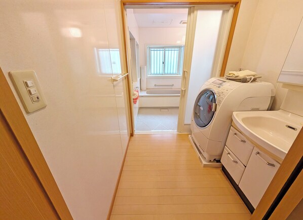 Quarto de hotel compacto com máquina de lavar, pia e pequena janela com persianas.
