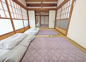 Una camera tradizionale in stile giapponese, con pavimento in tatami, due letti con coperte trapuntate, porte scorrevoli e soffitto in legno.