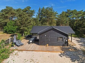 A cabin with a deck, outdoor seating, and a view of the surrounding forest. - 5 Star Holiday Home in Nexo (Nexø)