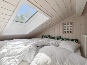 Ein Schlafzimmer mit Oberlicht, einem Bett mit weißer Bettwäsche und einem gerahmten Pflanzenprint an der Wand.