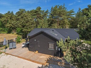 A cabin with a dark exterior, a sloped roof, and a wooden deck. - 5 Star Holiday Home in Nexo (Nexø)