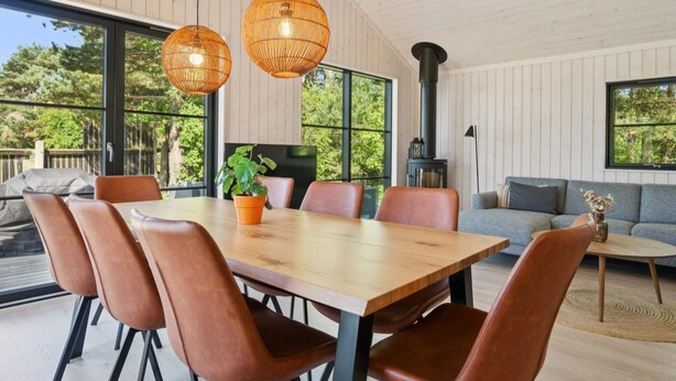 A modern dining area with a wooden table, leather chairs, and large windows offering a view of the outdoors. - 5 Star Holiday Home in Nexo (Nexø)
