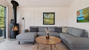A modern living room with a sectional sofa, a round wooden coffee table, a fireplace, and a large window with a view of trees. - 5 Star Holiday Home in Nexo (Nexø)