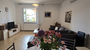 Ein Wohnzimmer mit einer Couch, einem Fernseher, einem Esstisch und Blumen.