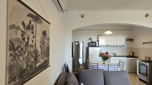 Une cuisine moderne équipée d’un réfrigérateur, d’une cuisinière et d’un four à micro-ondes. On y trouve une table à manger avec des chaises et un vase de fleurs. Un grand tableau encadré est accroché au mur.