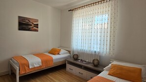 Une chambre avec deux lits simples, une petite table, une chaise et une fenêtre avec des rideaux.