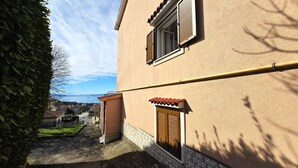 Un bâtiment avec un toit recouvert de tuiles, une fenêtre avec des volets et une tuyauterie apparente.
