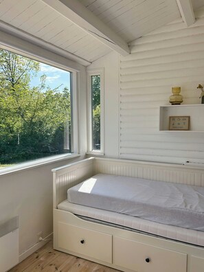Ein Zimmer mit Fenster, Bett, Heizkörper und einem Regal mit einer Vase.