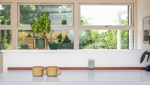 A kitchen with a white countertop, two mugs, a potted plant, and a window with a view of greenery. - Sea-view terrace on scenic Helgenæs (Knebel)