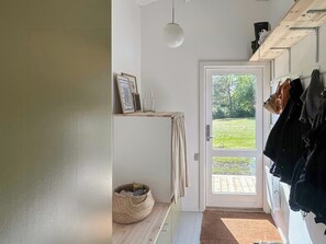 Ein Flur mit einer zur Garten führenden Tür, einer Pendelleuchte und einem Kleiderständer mit Gegenständen darauf.