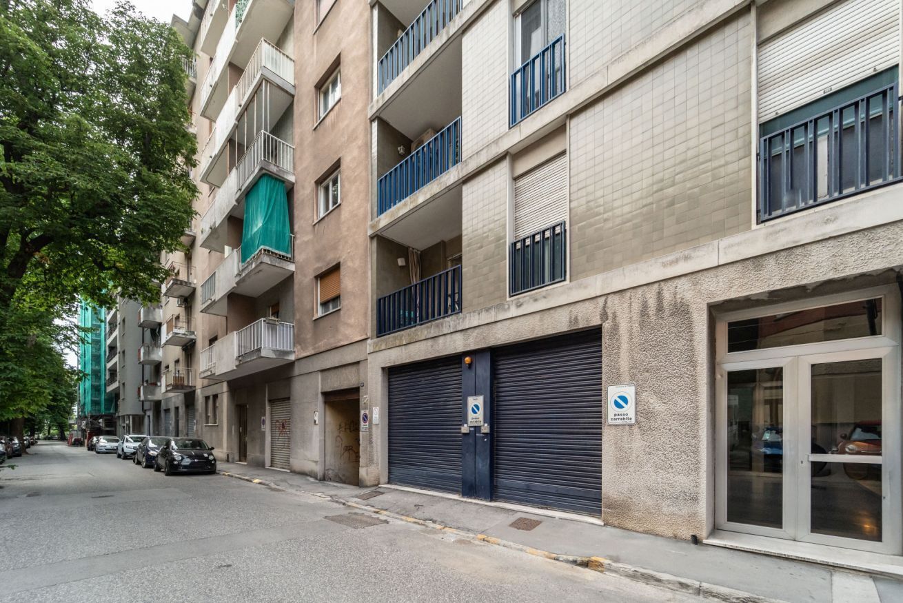 A multi-story residential building with balconies, a garage door, and parked cars.