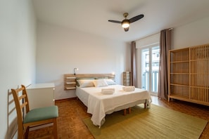 Ein Schlafzimmer mit Bett, Schreibtisch, Stuhl, Deckenventilator, Fenster und Kleiderschrank.