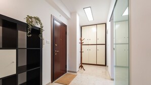 A hallway with a wooden door, a black shelving unit, a plant, a wooden coat stand, and a sliding glass door leading to a room. - GuestHost - Comfy Flat X4 Near the Center (Trieste)