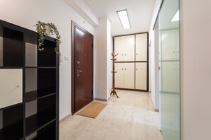Ein Flur mit Holztür, einem schwarzen Regalelement, einer Pflanze, einem Holz-Kleiderständer und einer Schiebetür zu einem Zimmer.