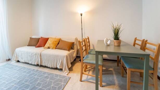 A bedroom with a bed, bedside table, lamp, and a dining area with a table and chairs. - GuestHost - Comfy Flat X4 Near the Center (Trieste)