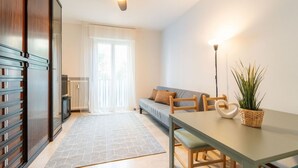 A modern living room with a sofa, a dining table, a ceiling fan, and a radiator. - GuestHost - Comfy Flat X4 Near the Center (Trieste)