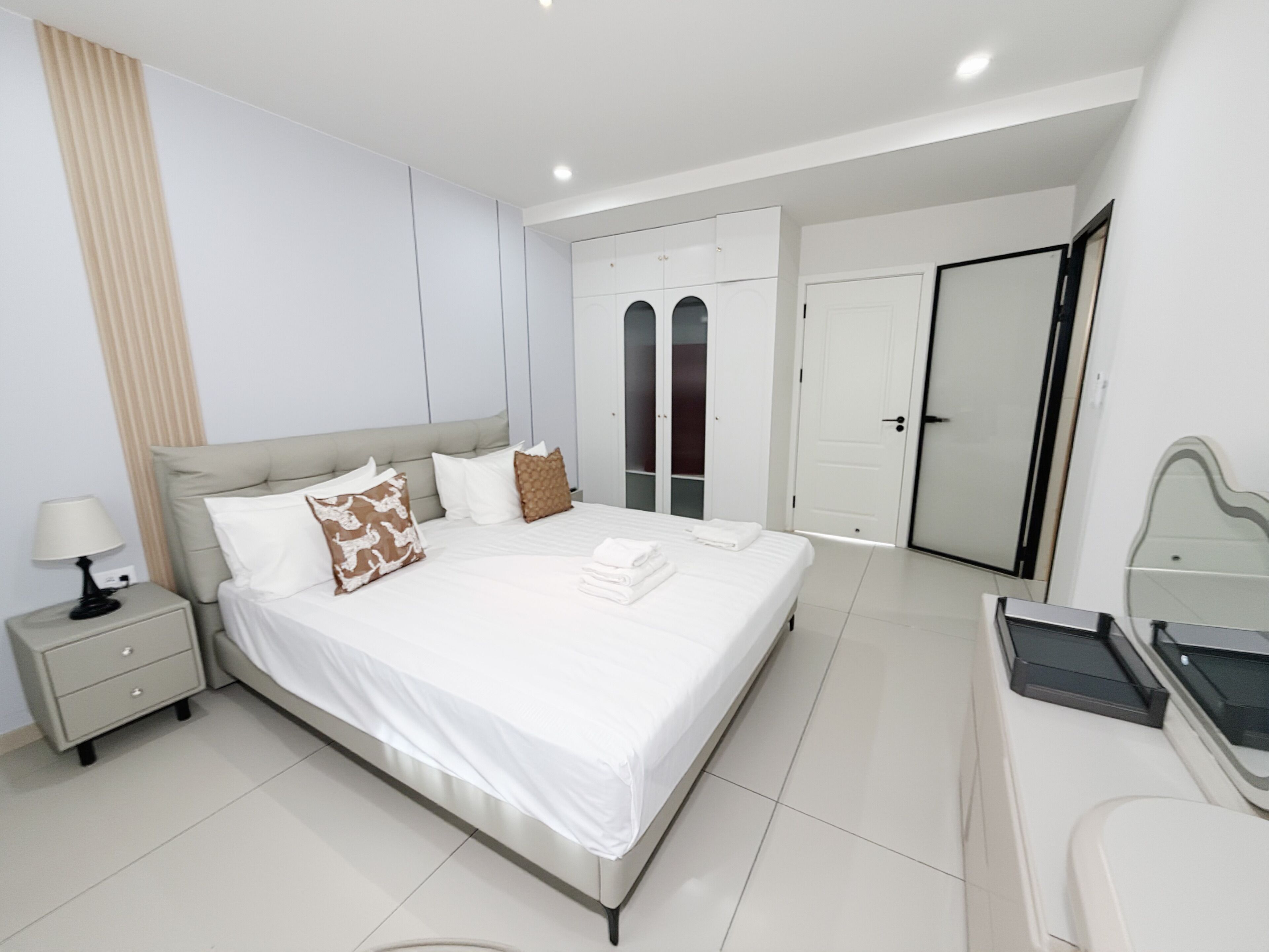 A modern bedroom with a large bed, bedside tables, a wardrobe, and a mirror.