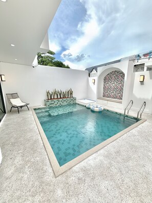 En swimmingpool med fliseterrasse, liggestol og en dekorativ væg med blomstermønster.